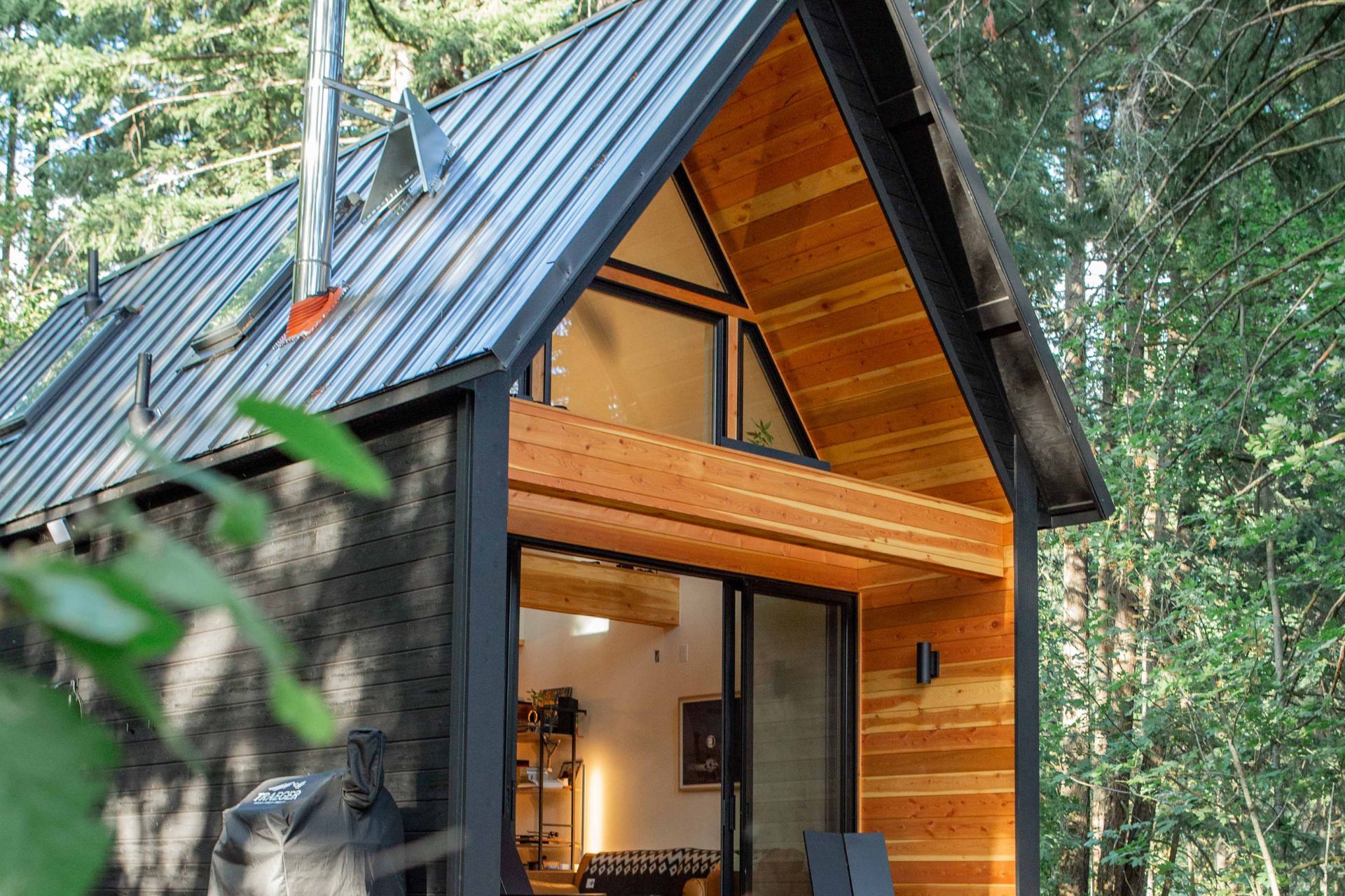 Schwarzes Holzhaus mit hellen kontrastierenden Details in einem Wald