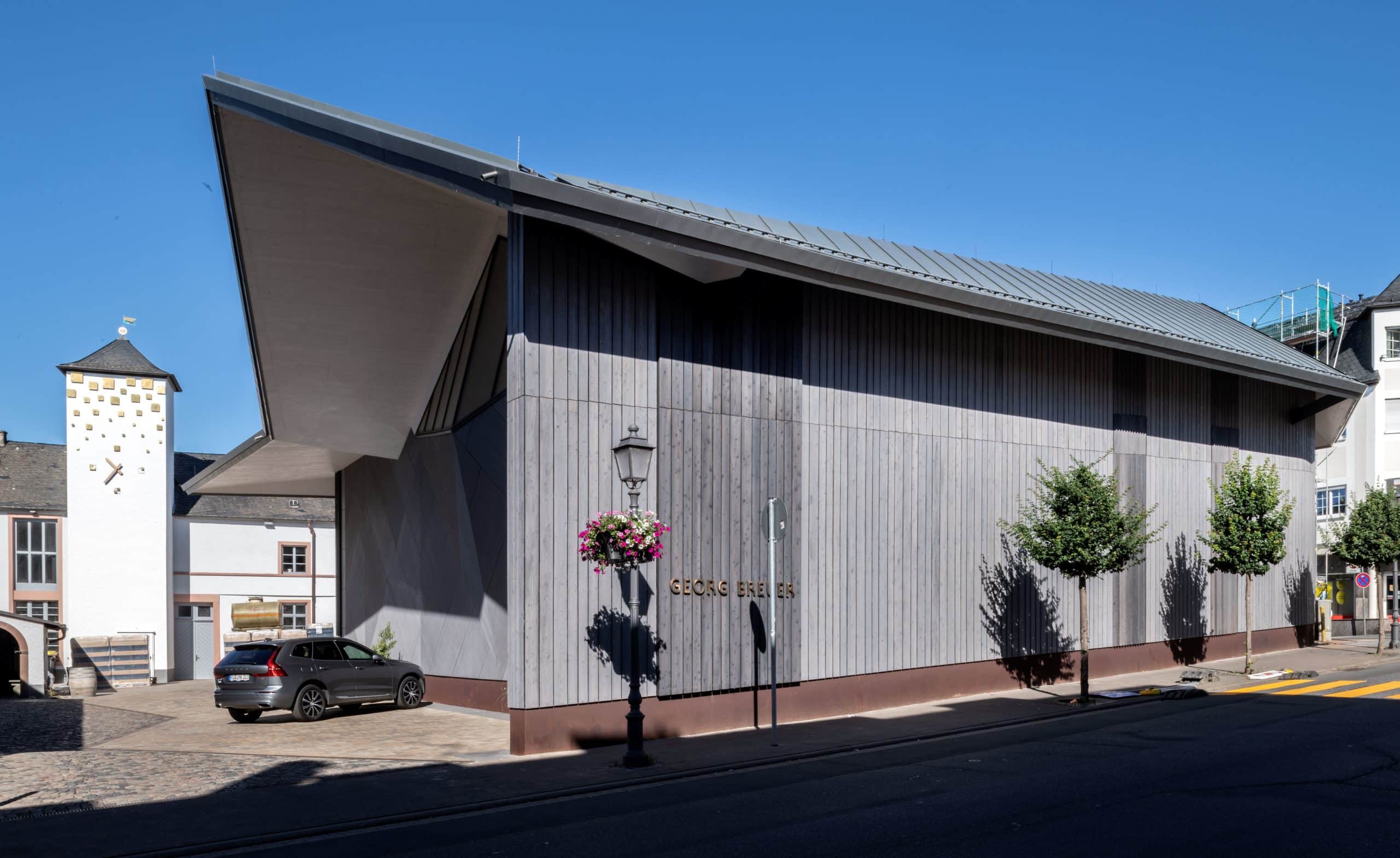 Building with grey cladding wood, blue sky and car in the background